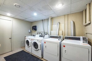 Une buanderie équipée de trois machines à laver et d’un sèche-linge, d’un distributeur noir fixé au mur et d’une conduite de ventilation.