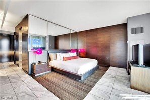 Una habitación de hotel moderna con una cama grande, un armario, un televisor y un espejo amplio.
