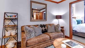 En hyggelig stue med en brun lædersofa, puder med mønster, et træsofabord og en kommode med glas og service.