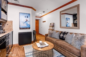 A living room with a brown sofa, a coffee table, and a poster on the wall. There is a door leading to another room and a small table with a picture frame. - Westgate 4916-b (Park City)