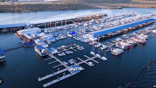 An aerial view of a marina with numerous boats docked, a large covered structure, and a distant mountain range. - 119th Sun City (Sun City)