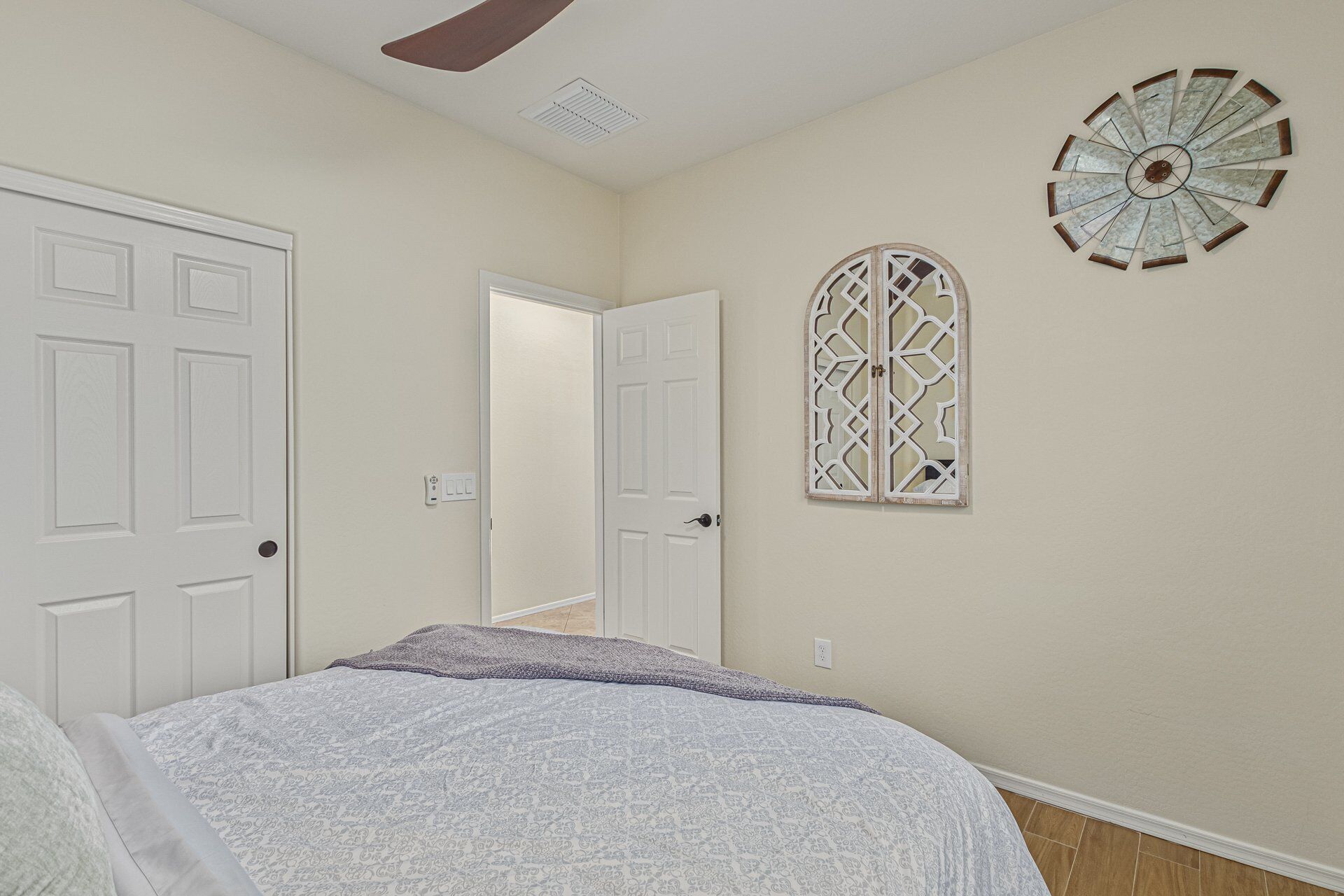 A bedroom with a bed, a ceiling fan, a decorative wall piece, and a door leading to another room.