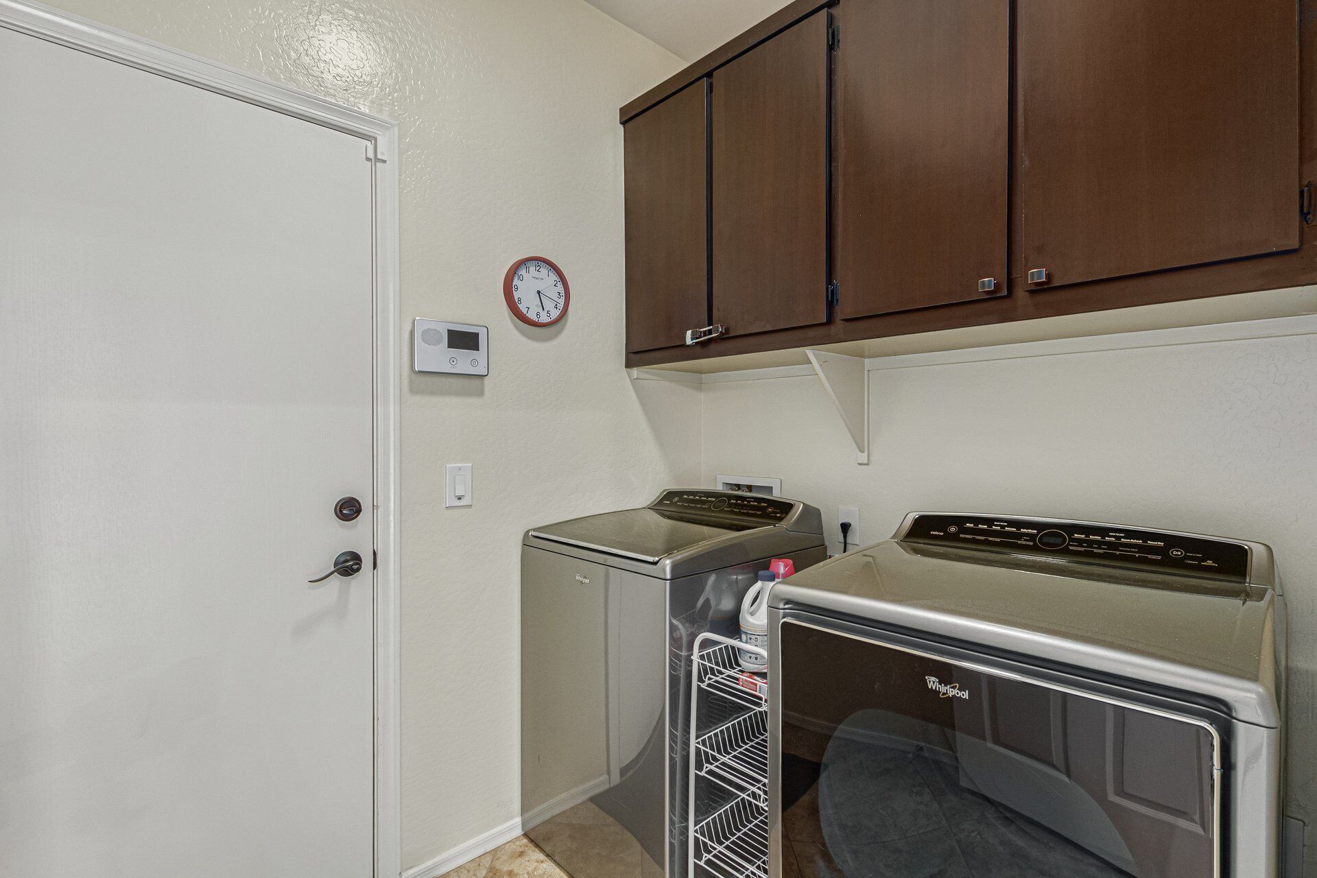 A laundry room with a washer and dryer, a clock, and wooden cabinets above.