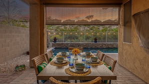 An outdoor dining area with a pool, wicker furniture, and a view of a desert landscape. - 119th Sun City (Sun City)