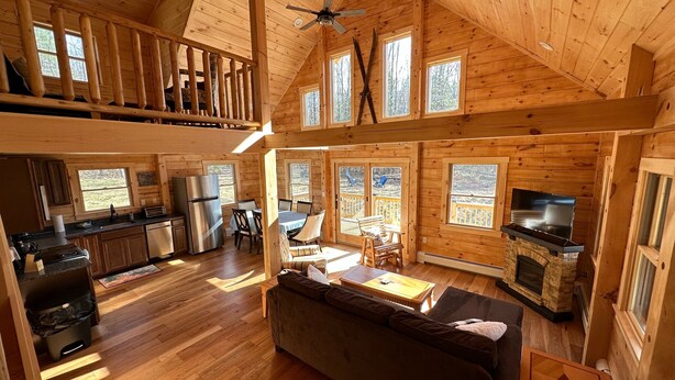 A spacious cabin with a high ceiling, wooden interior, a dining area, kitchen, and a fireplace. - 18ha Log Home Close to Franconia Notch Privacy, Fire Pit, Wifi, Pool gym Passes (Sugar Hill)