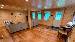 A wooden cabin interior with a sofa, a dining table, and a chair. - 18ha Log Home Close to Franconia Notch Privacy, Fire Pit, Wifi, Pool gym Passes (Sugar Hill)