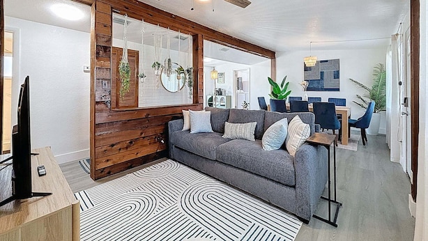 A living room with a grey sofa, a ceiling fan, hanging plants, and a dining area in the background. - Modern 3 Bedroom Retreat With Pool & Fire Pit (Largo)
