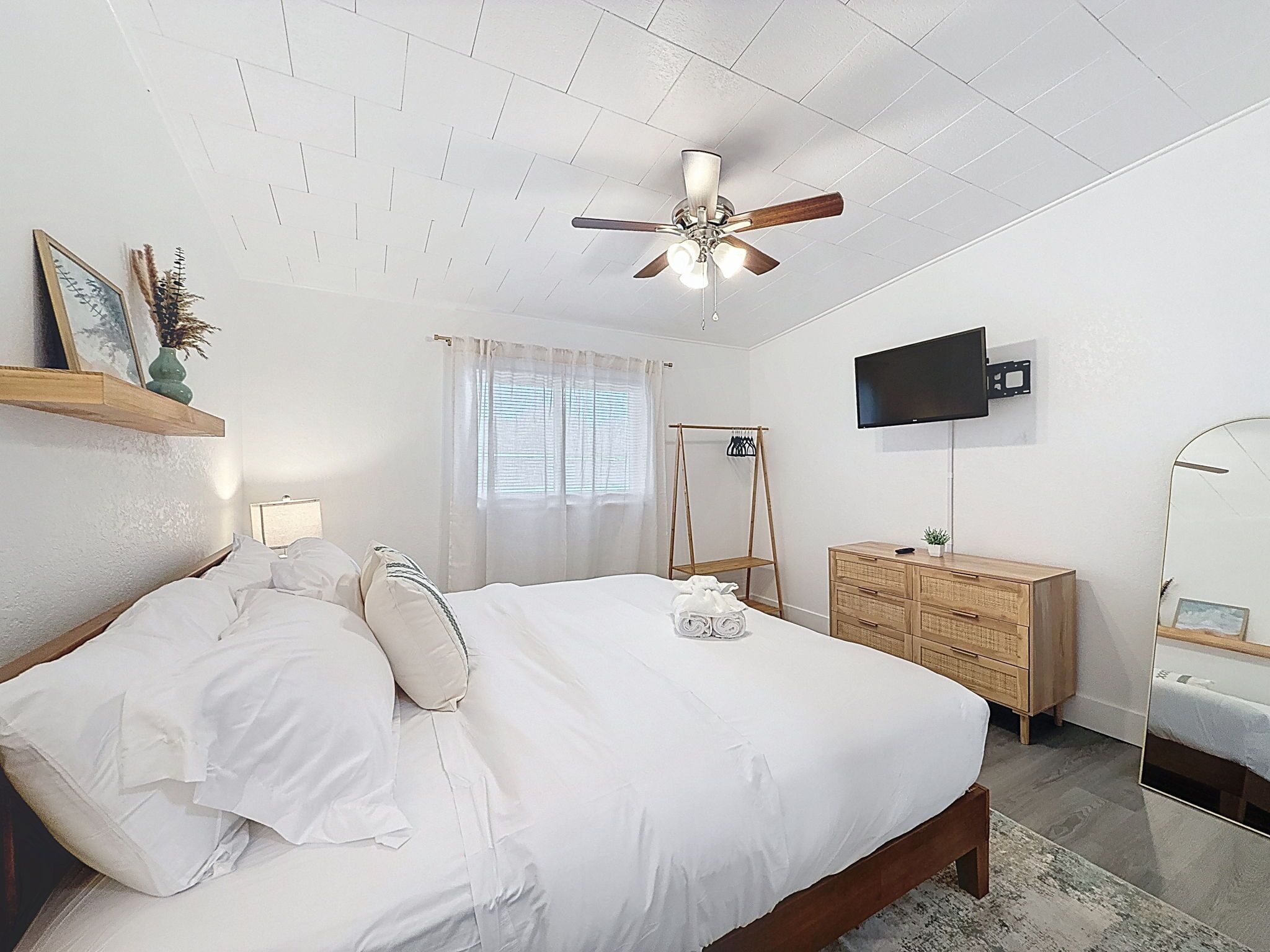 Ein Schlafzimmer mit einem Bett, einer Holzkommode, einem Fernseher und einem Deckenventilator.