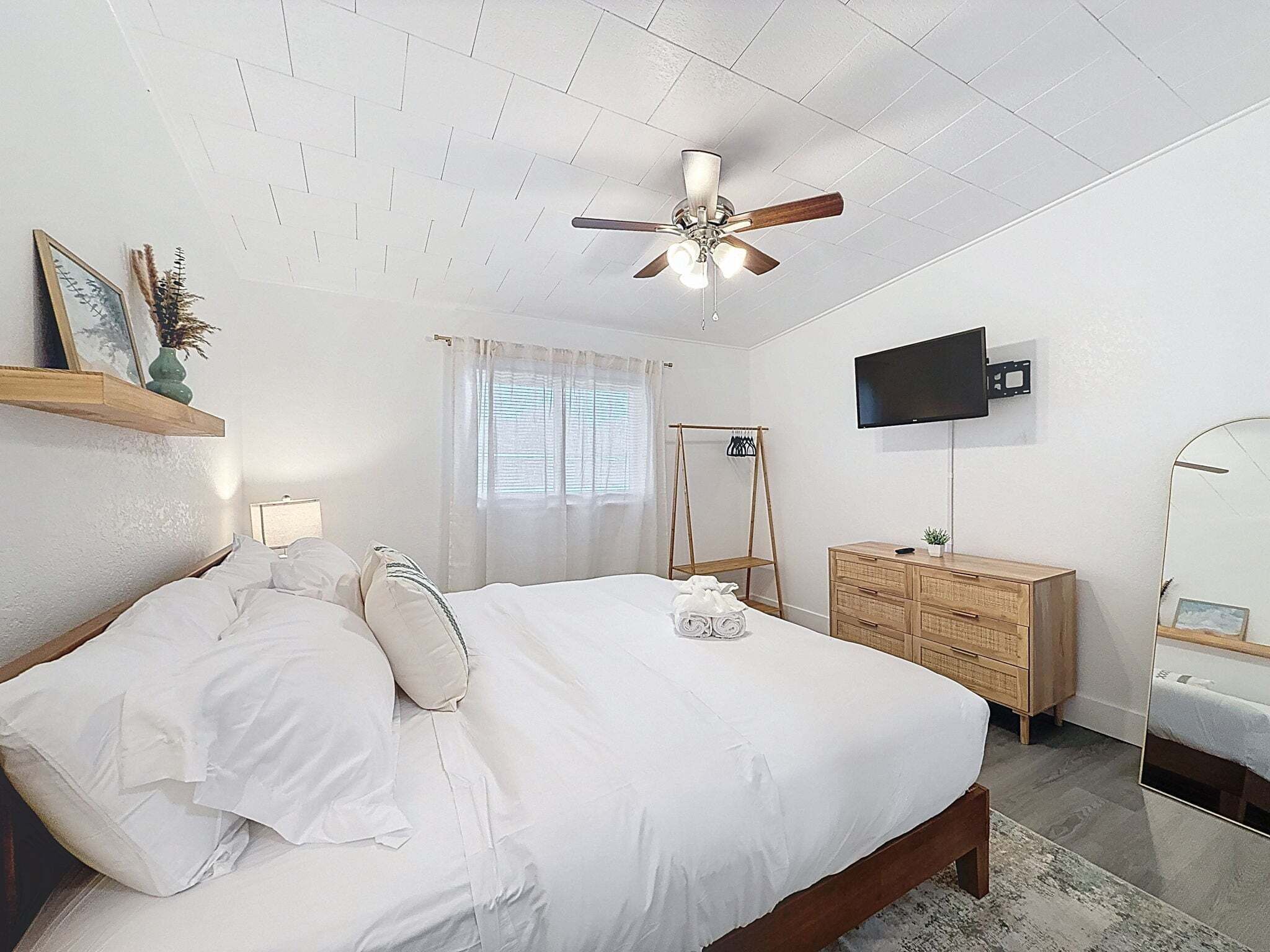 Un dormitorio con cama, ventilador de techo, televisor, cómoda y ventana con cortinas.