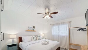 A bedroom with a bed, bedside tables, a ceiling fan, a window with curtains, and a coat rack. - Modern 3 Bedroom Retreat With Pool & Fire Pit (Largo)