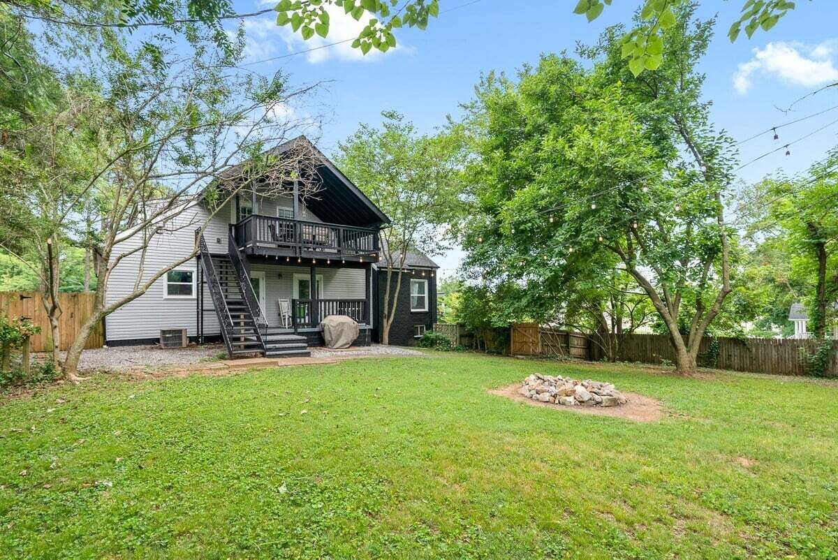 Een huis met twee verdiepingen, met een balkon, omgeven door een verzorgd gazon en bomen.