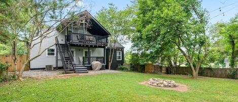 Een huis met twee verdiepingen, met een balkon, omgeven door een verzorgd gazon en bomen.