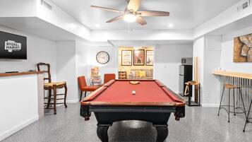 A pool table in a room with white walls, a ceiling fan, and a clock.