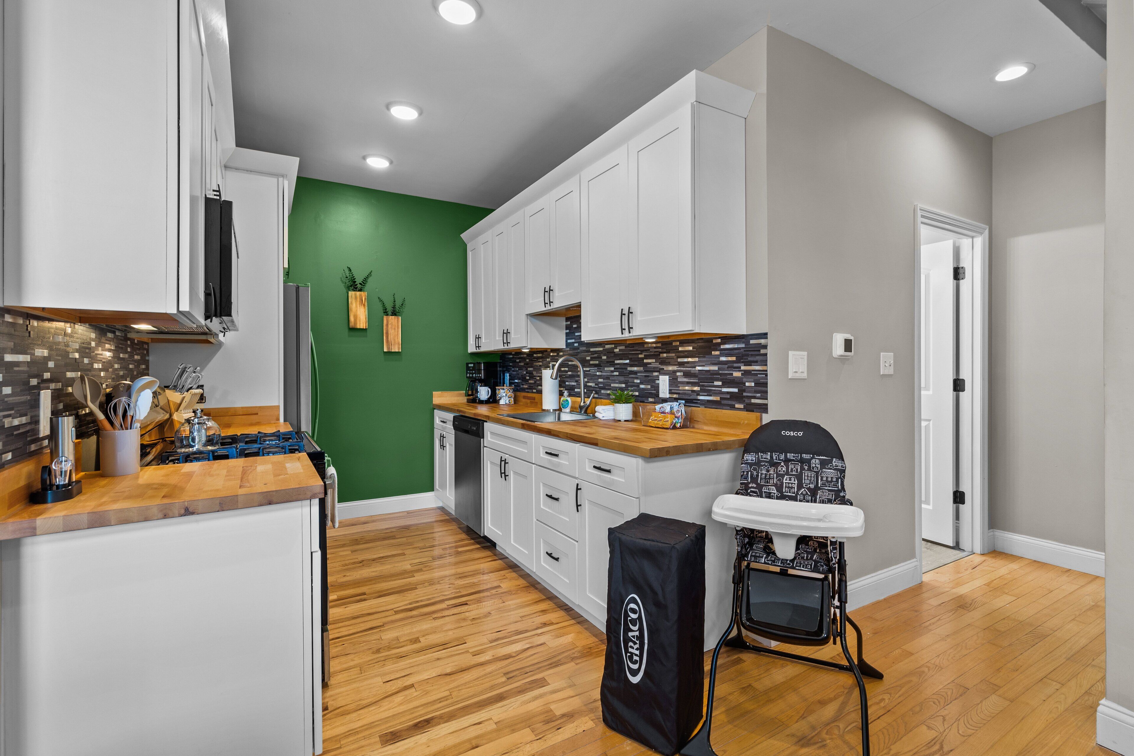 A modern kitchen with white cabinets, a wooden countertop, and a green accent wall.