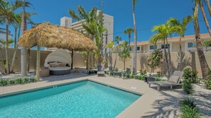 A pool area with a thatched-roof seating area, lounge chairs, and a clear blue pool. - A Shell House Compound (Siesta Key)