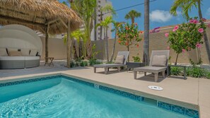A swimming pool with lounge chairs and a thatched-roof structure. - A Shell House Compound (Siesta Key)