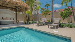 A poolside area with lounge chairs, a thatched umbrella, and tropical plants. - A Shell House Compound (Siesta Key)