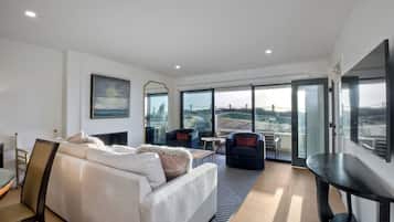 A modern living room with a sofa, chairs, a table, and large windows offering a view of the cityscape.