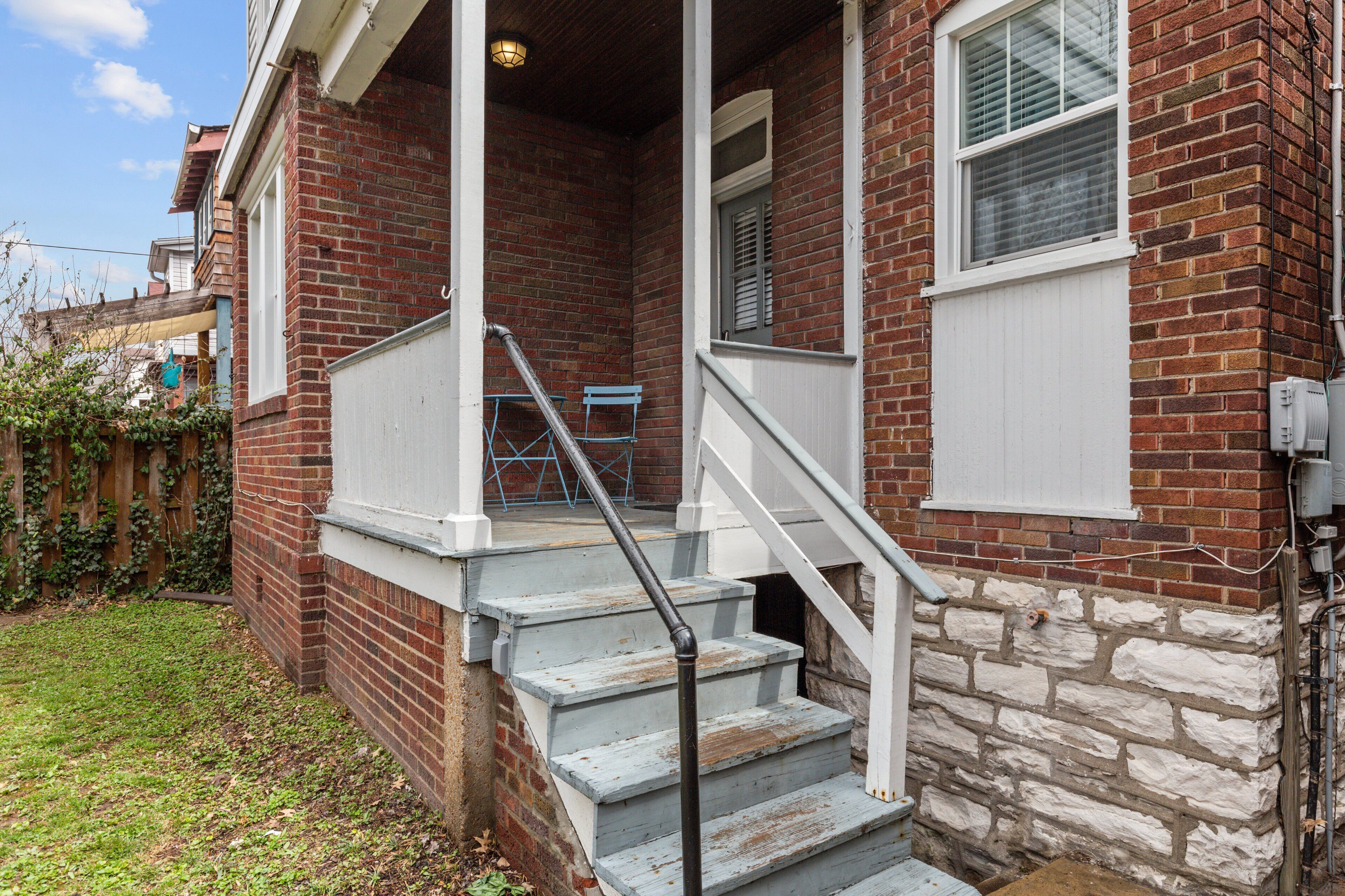 A brick house with a porch, a set of stairs, and a small table.