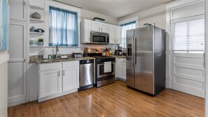 Una cocina con armarios blancos, electrodomésticos de acero inoxidable y suelo de madera.