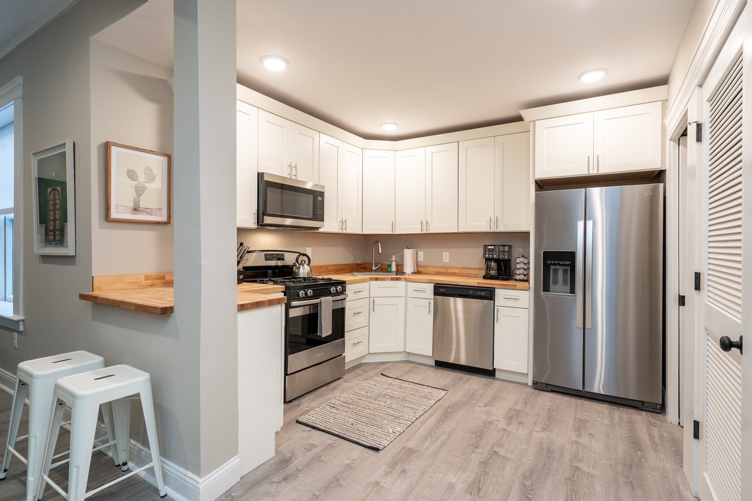 A modern kitchen with white cabinets, stainless steel appliances, and a wooden countertop.