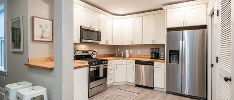 A modern kitchen with white cabinets, stainless steel appliances, and a wooden countertop.