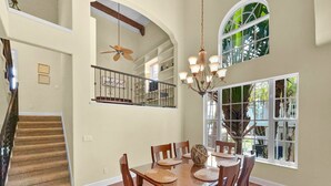 A spacious dining area with a high ceiling, a staircase, and large windows. - Avenida De Cortez (Siesta Key)