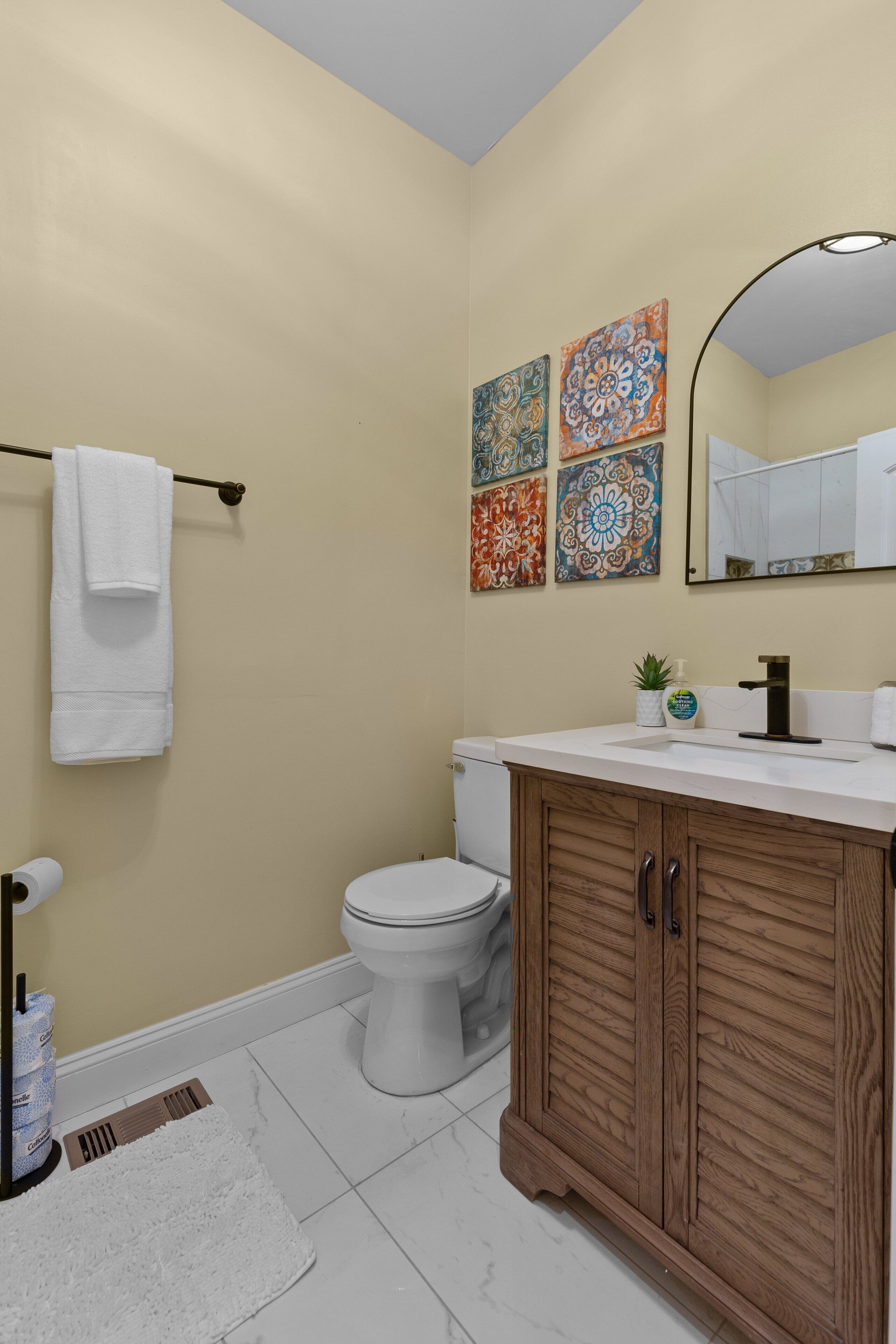 Une salle de bain comprenant des toilettes, un lavabo, un meuble en bois, un porte-serviettes et des carreaux décoratifs.