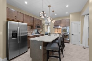 A modern kitchen with stainless steel appliances, wooden cabinets, and a central island with bar stools. - Red Brick Hideaway (St. Louis)