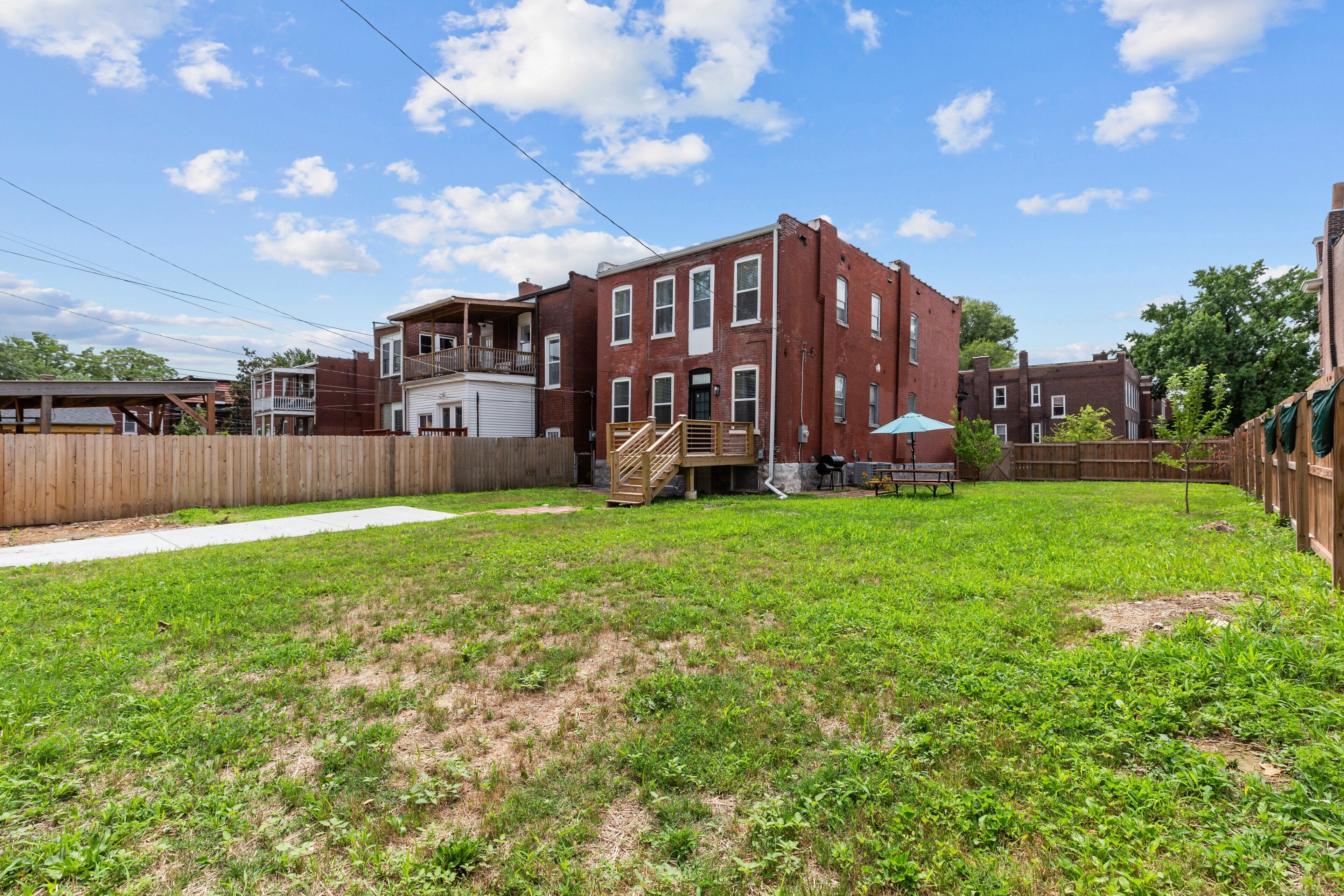 A spacious backyard with a wooden fence, a brick building, and a clear sky.