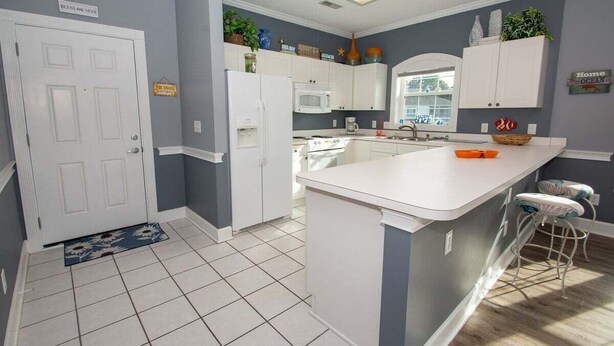 A kitchen with white cabinets, a central island, a microwave, and a sink. - River Walk 301 (Myrtle Beach)
