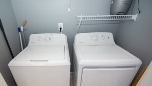 A laundry room with two white front-loading washing machines, a drying rack above, and a mop on the left. - River Walk 301 (Myrtle Beach)