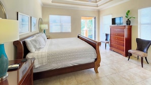 Une chambre à coucher comprenant un lit, une commode, une chaise, un téléviseur et un ventilateur de plafond.