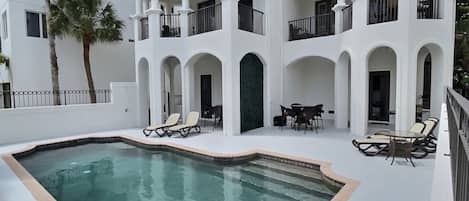A poolside area with lounge chairs and a pool, surrounded by a white building with balconies.