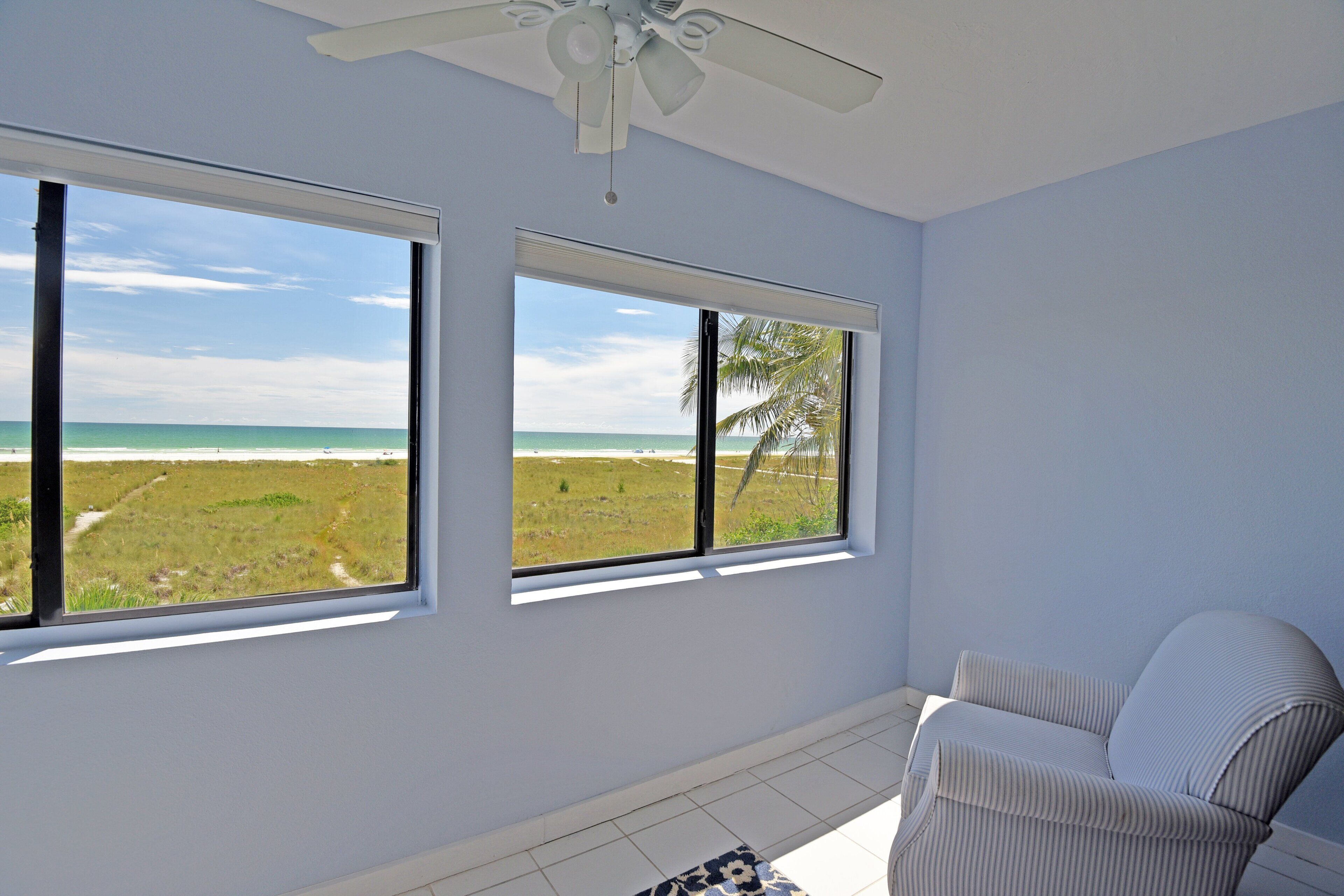 A room with two large windows offering a view of the beach and ocean.