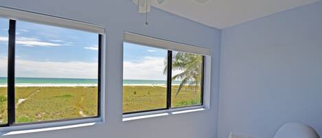A room with two large windows offering a view of the beach and ocean.