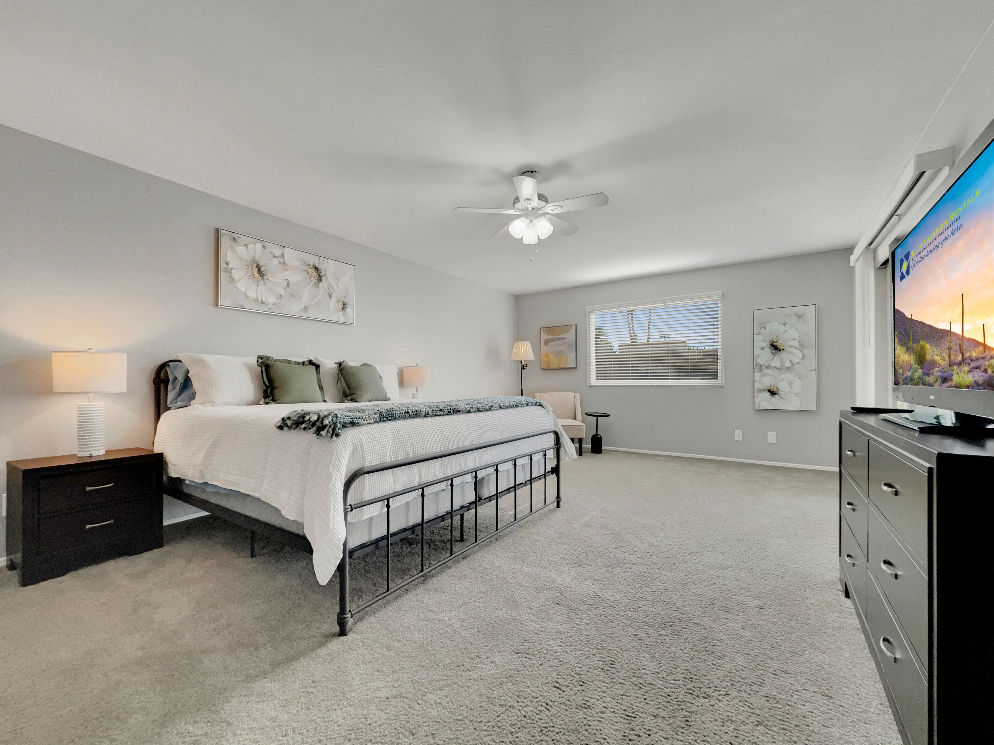 A bedroom with a bed, bedside tables, a ceiling fan, a dresser, and a TV.