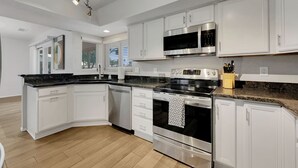 Cocina moderna con armarios blancos, electrodomésticos de acero inoxidable y encimera de granito.