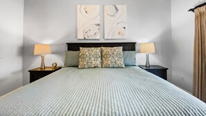 A bedroom with a large bed, two nightstands, two lamps, and two abstract paintings on the wall. - Bayside Pointe - 1232 (Siesta Key)