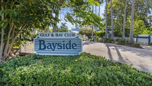 A sign for Gulf & Bay Club Bayside with a well-maintained garden and palm trees in the background. - Bayside Pointe - 1232 (Siesta Key)