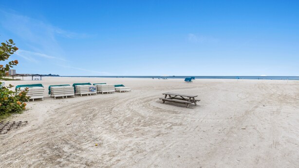 A sandy beach with picnic tables and lounge chairs. - Siesta Beach House 203 Sunny Daze (Siesta Key)