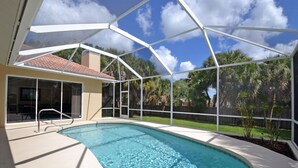 Une piscine dotée d’une zone abritée, avec une eau d’un bleu limpide, et offrant une vue sur une maison et des palmiers en arrière-plan.