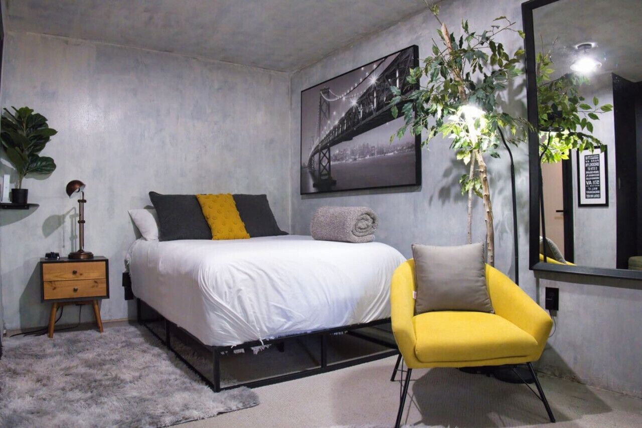 Une chambre à coucher comprenant un lit, une table de chevet, une lampe, une chaise et un grand miroir.
