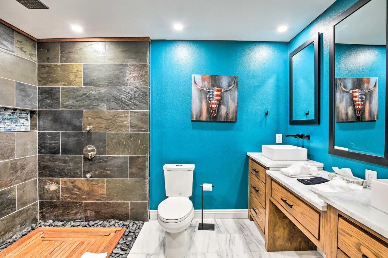 Un baño con pared azul, inodoro blanco, lavabo y espejo.