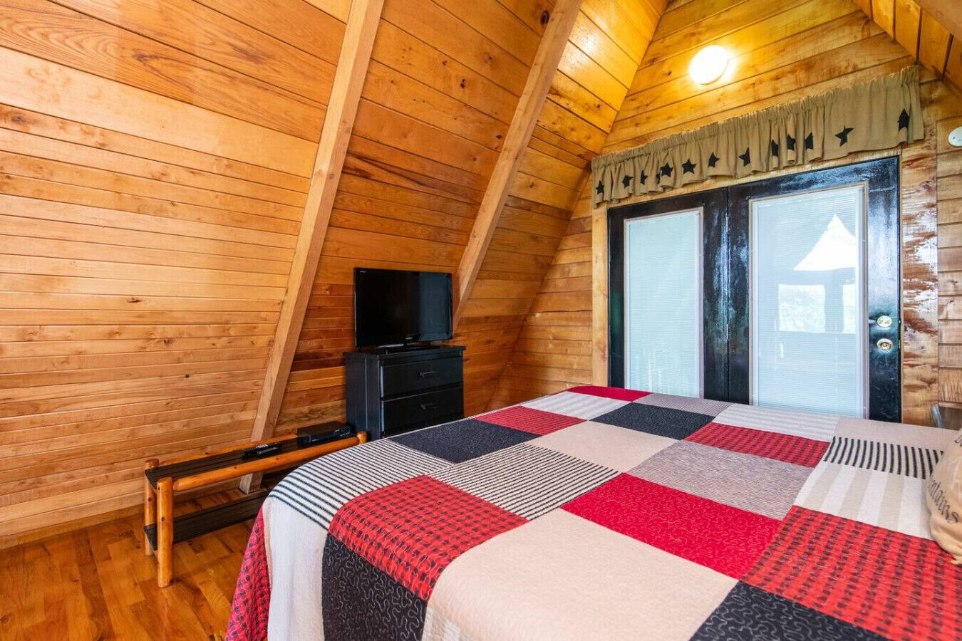 A cozy wooden cabin room with a bed, a television, and a window.