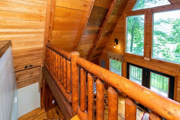 A wooden staircase with a railing leading to a room with large windows and a view of greenery outside. - Hot Tub - Haven at the Red - Red River Gorge, KY (Stanton)
