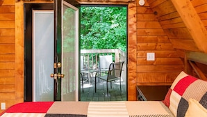 Ein Zimmer in einer Holzhütte mit einem Bett, einem Fenster und einer Tür zu einer Terrasse mit Stühlen.