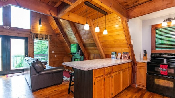 Ein gemütliches Blockhaus-Interieur mit Holzausstattung, einer Küchenzeile mit Herd und Backofen, einem Essbereich mit Tisch und Stühlen und einem großen Fenster, das für natürliches Licht sorgt.