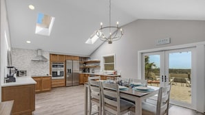 A modern kitchen with wooden cabinets, a central island, and a dining area with chairs. - Sea-esta (Siesta Key)