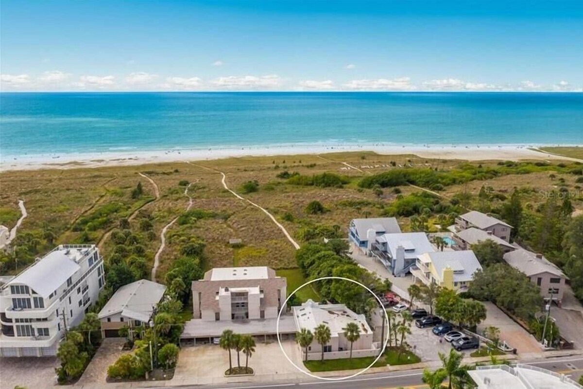 An aerial view of a coastal area with buildings, a beach, and a road.